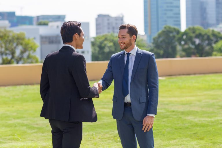 An international CEO and a Guinean entrepreneur shaking hands in front of the headquarters, symbolizing the success of Yes Invest in Guinea partnerships.
